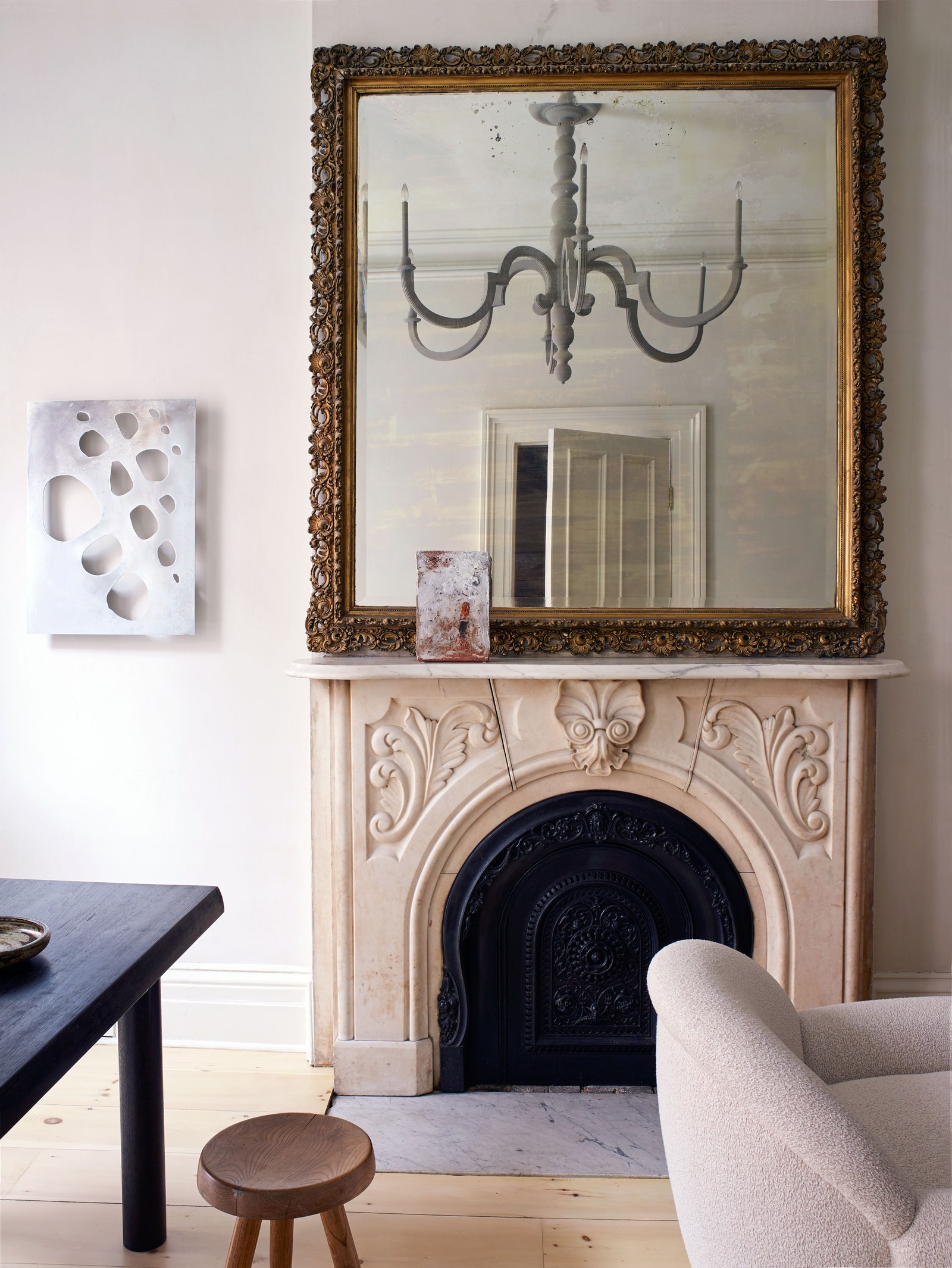 a living room mantle with with an ornate mirror and a chandelier and a black dining table