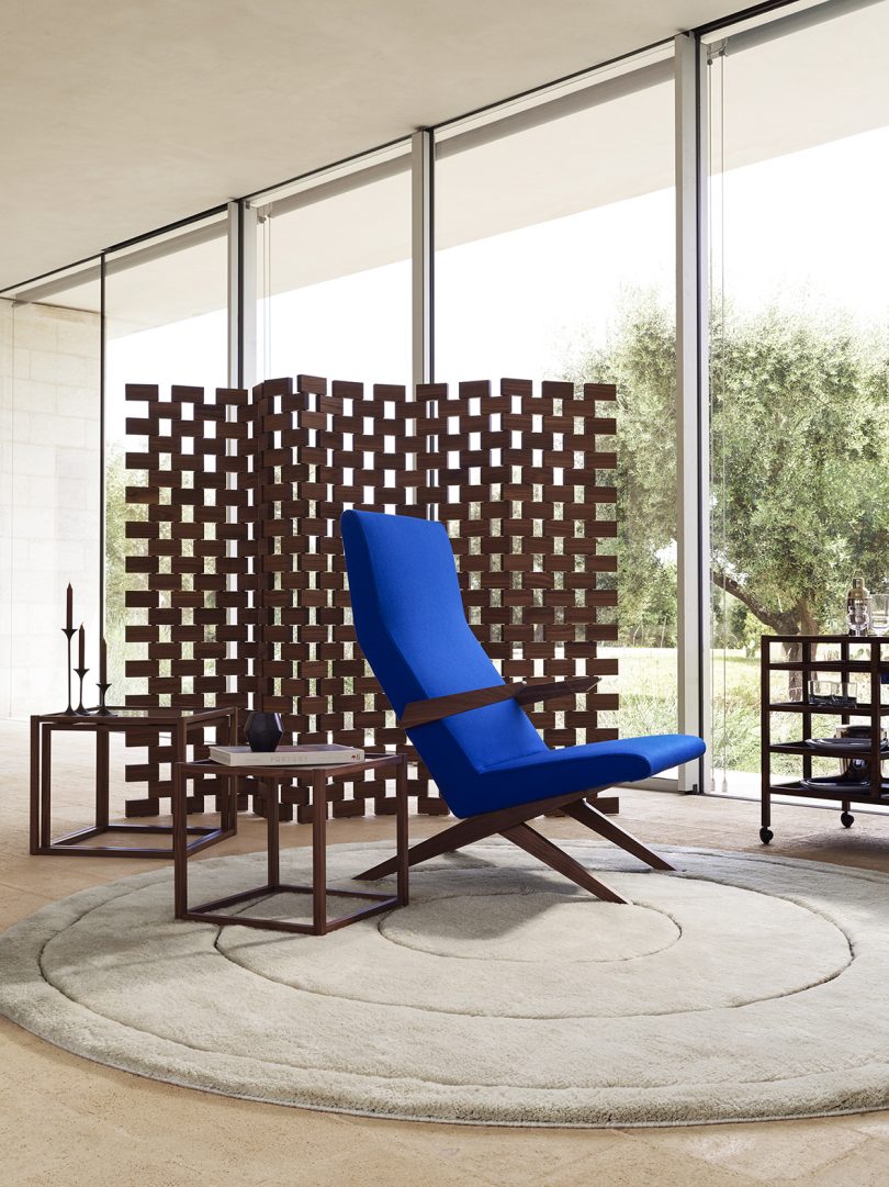 bright blue armchair, side tables, service trolley, and privacy screen in front of a wall of windows