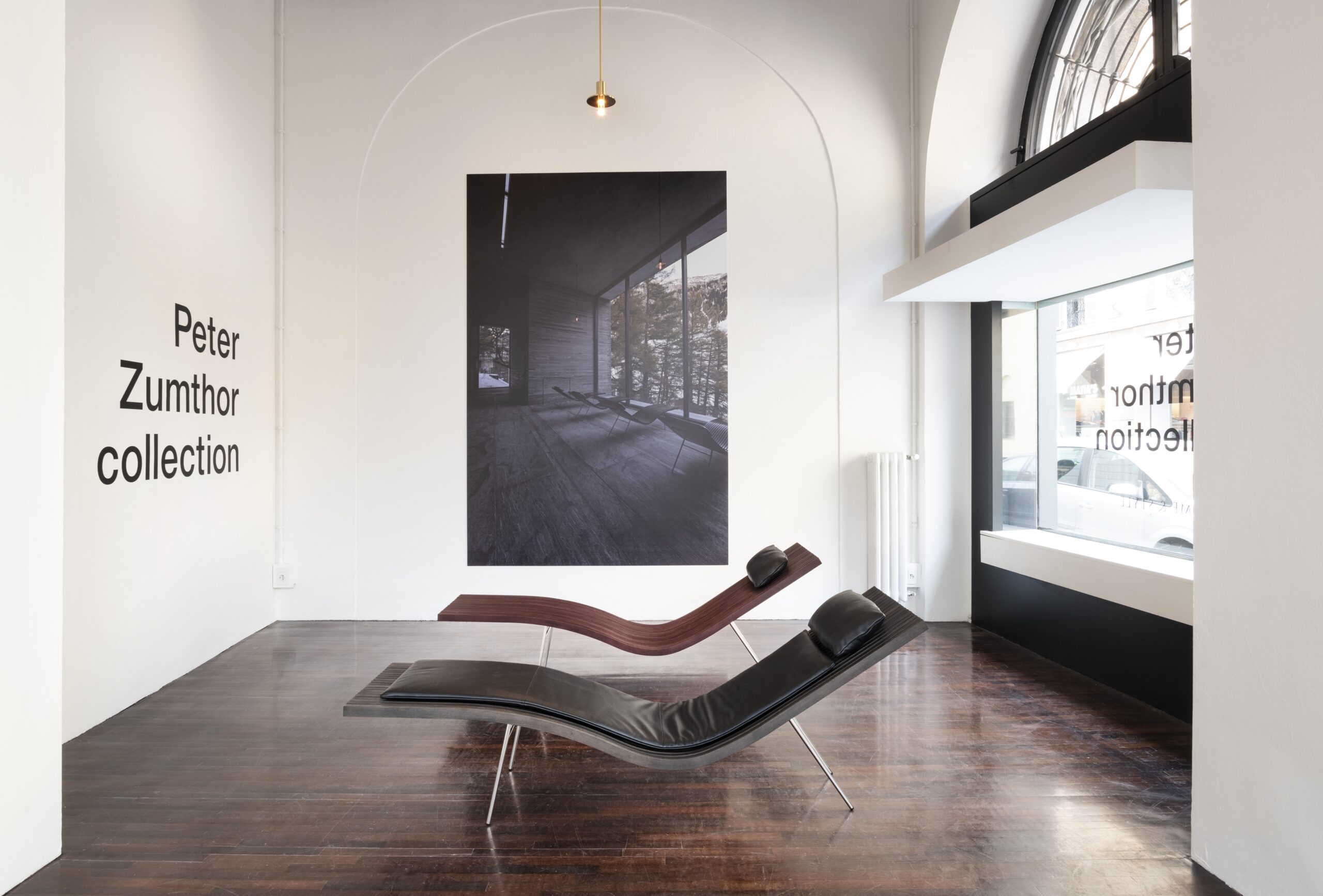 Image of two chaise lounge chairs in a showroom with a wall that reads "peter zumthor collection" 