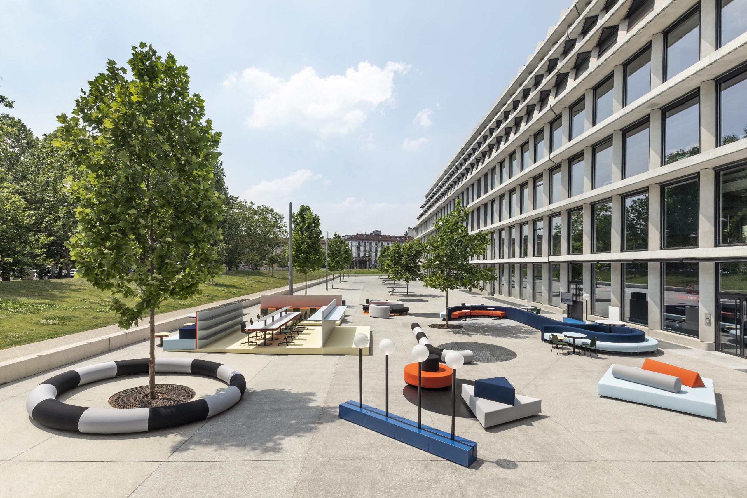 Image of a collection of furniture outdoor in a plaza in between a building and trees